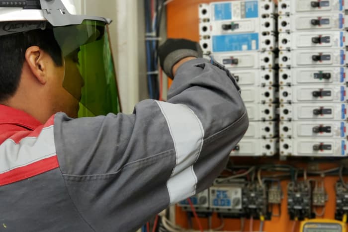 Técnico medindo grandezas elétricas em um quadro de comando