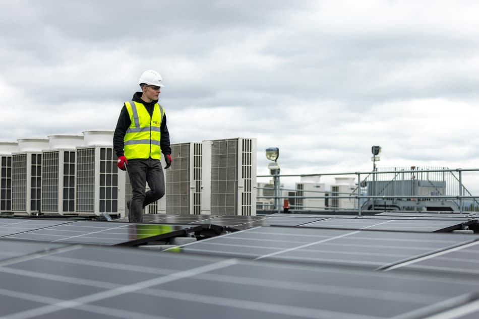 Técnico caminhando em cobertura de prédio entre equipamentos de climatização